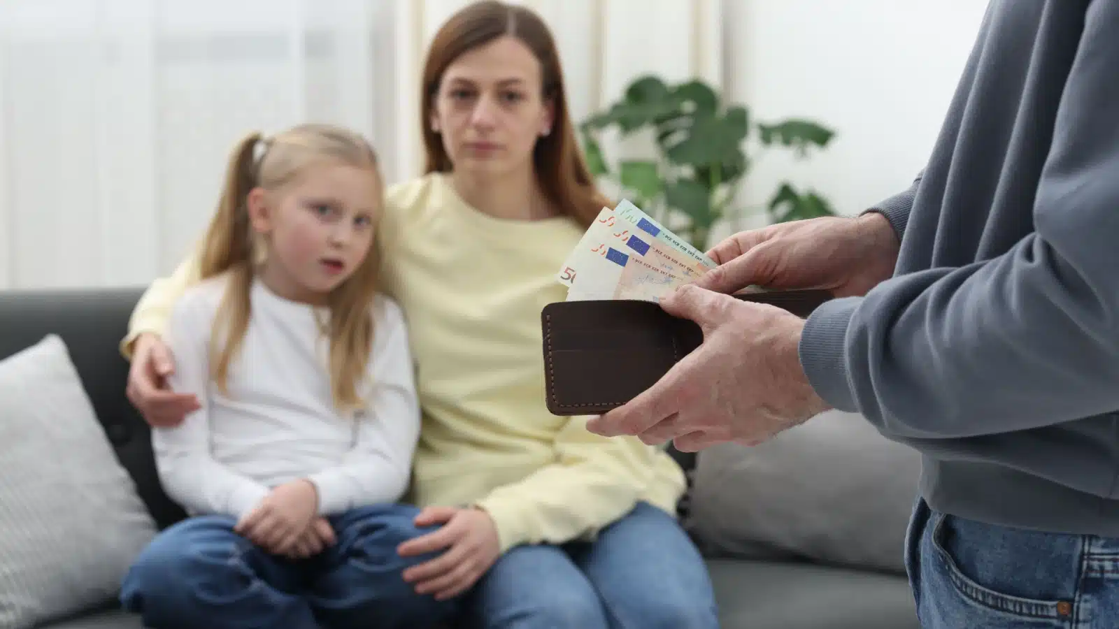 A man takes money from his wallet to give to his sad ex-wife and daughter for child support.
