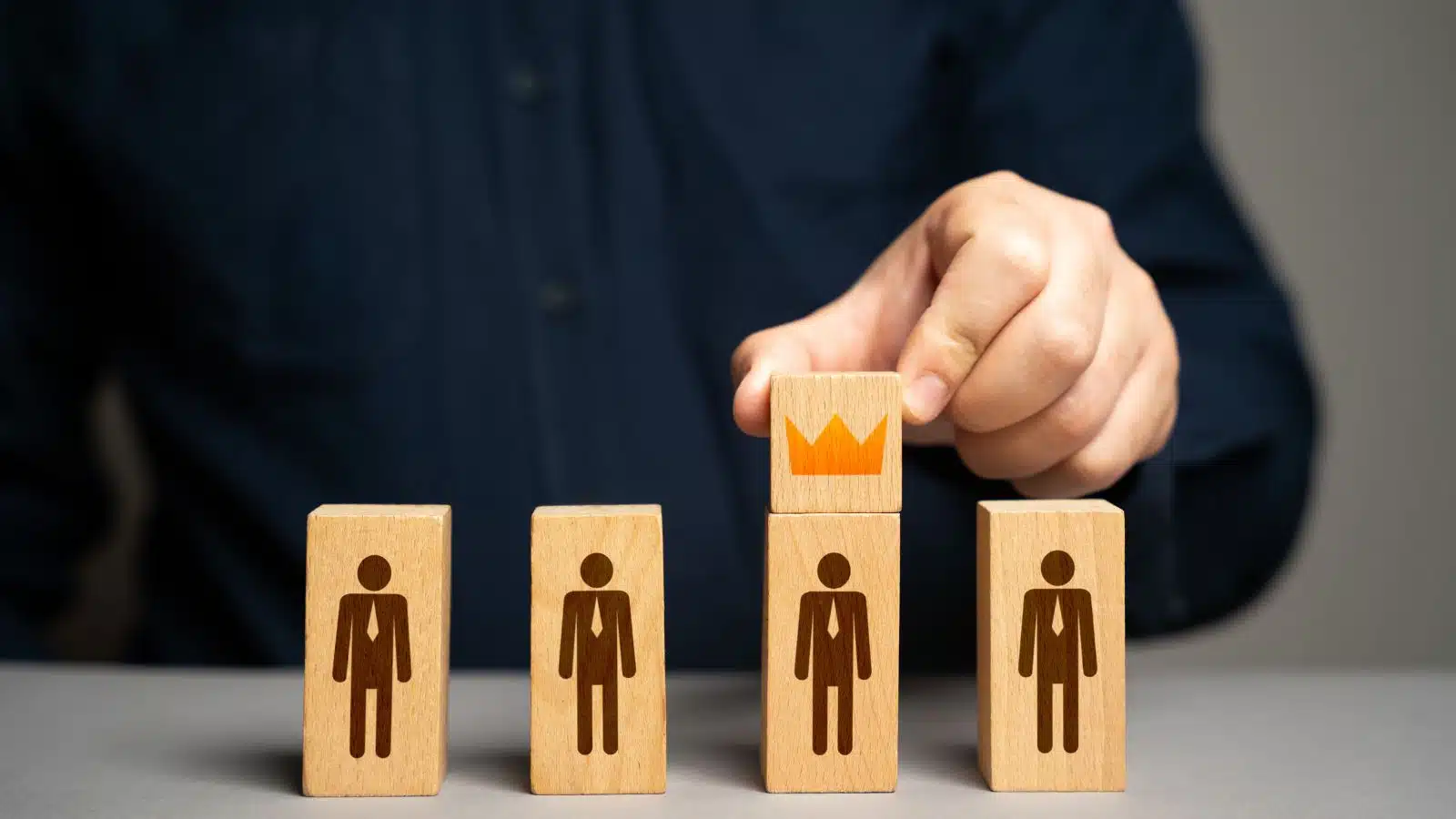 A boss plays favorites with employees by placing a crown on a wooden model of one worker.