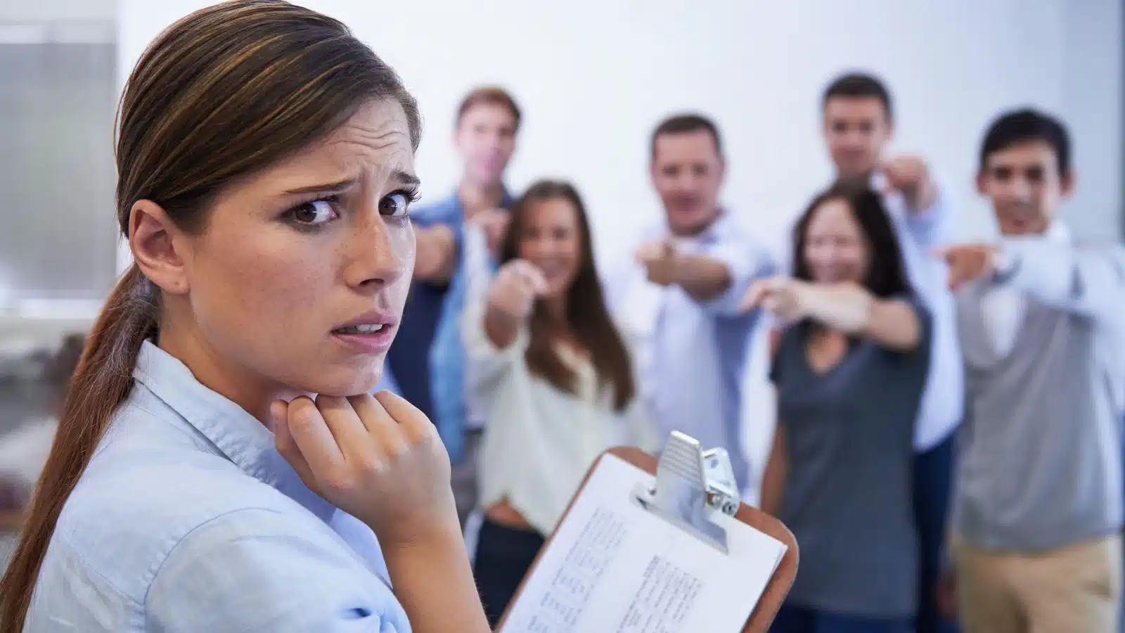 Office workers all point and laugh at the new person, who looks anxious, to represent signs of a toxic workplace.