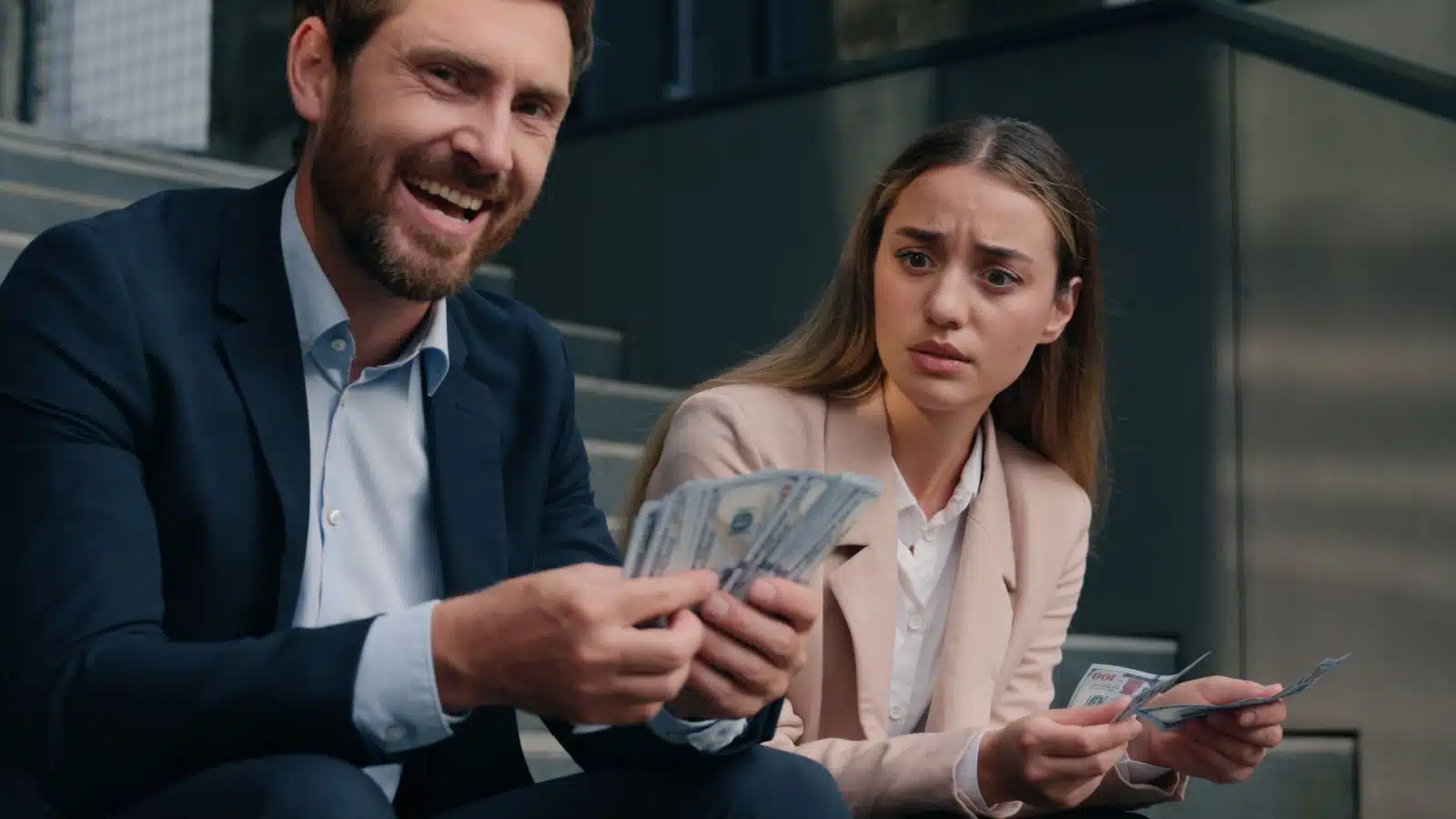A business man and business women sitting on the steps counting their money. The man has more to represent a glaring example of sexism: the gender pay gap. 