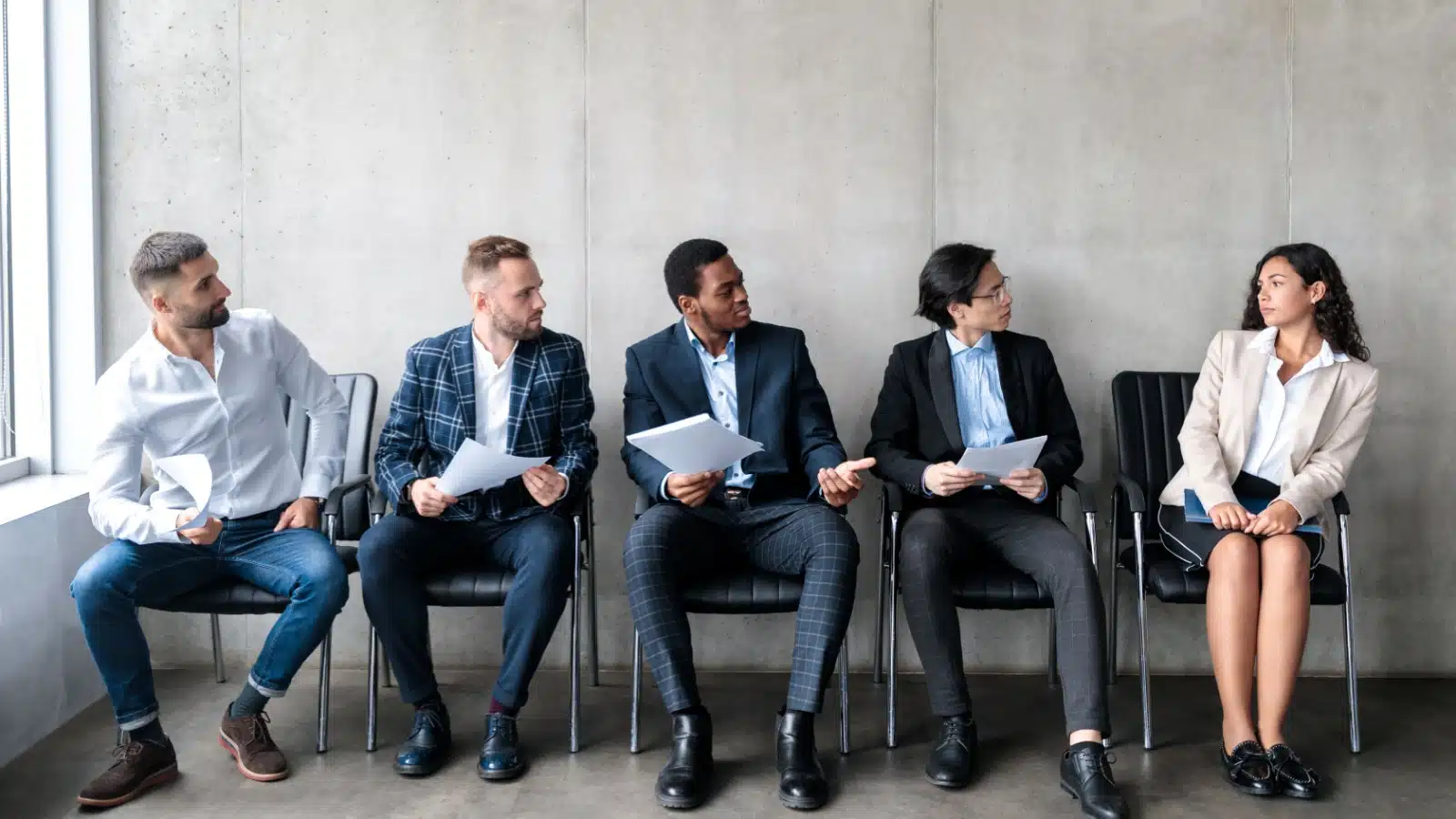 Four men and five women are waiting for an interview. All the men are staring at the uncomfortable woman to represent sexism examples in the workforce.