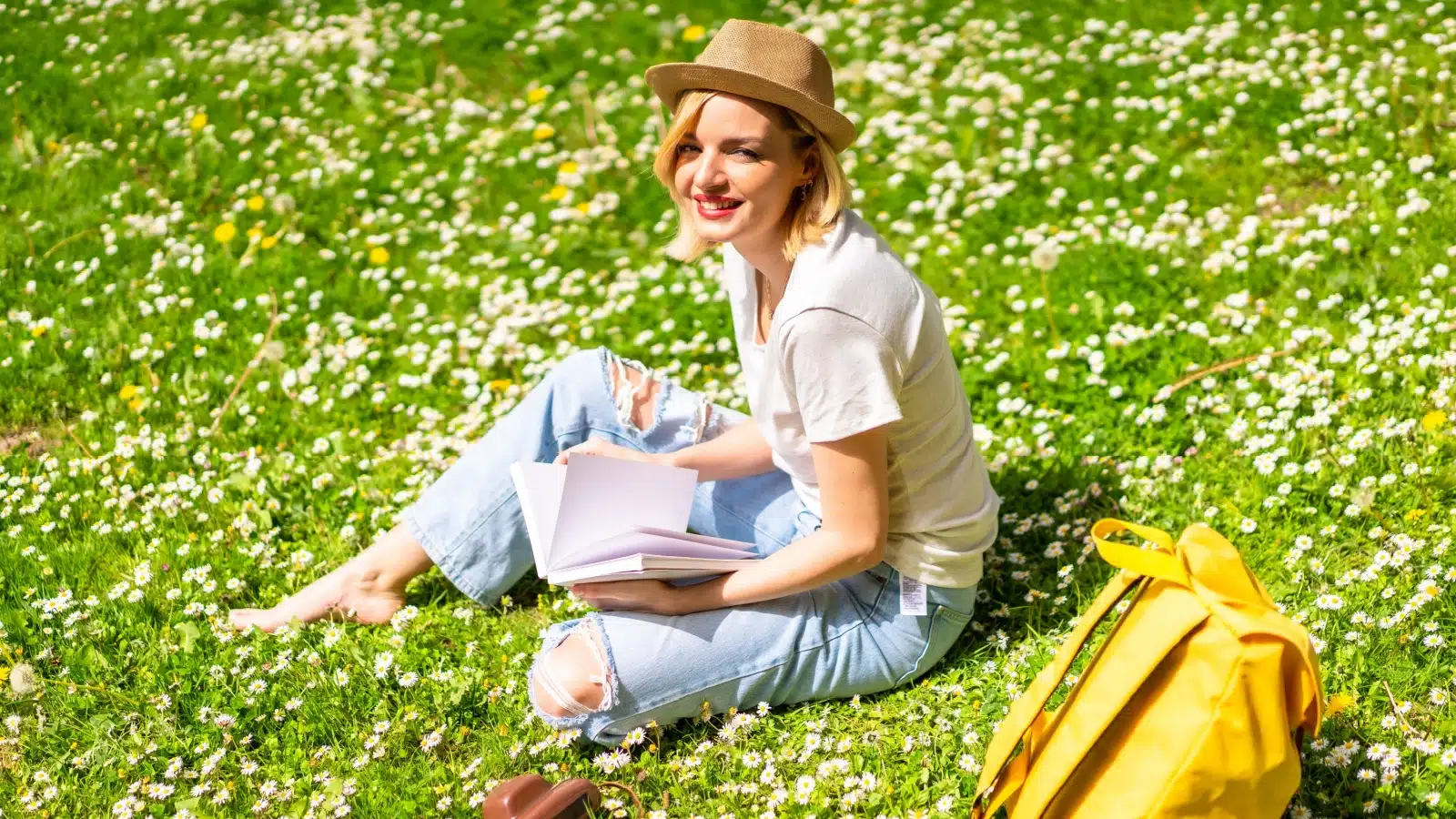 A woman sitting in a grassy field with a book to represent summer poems. 