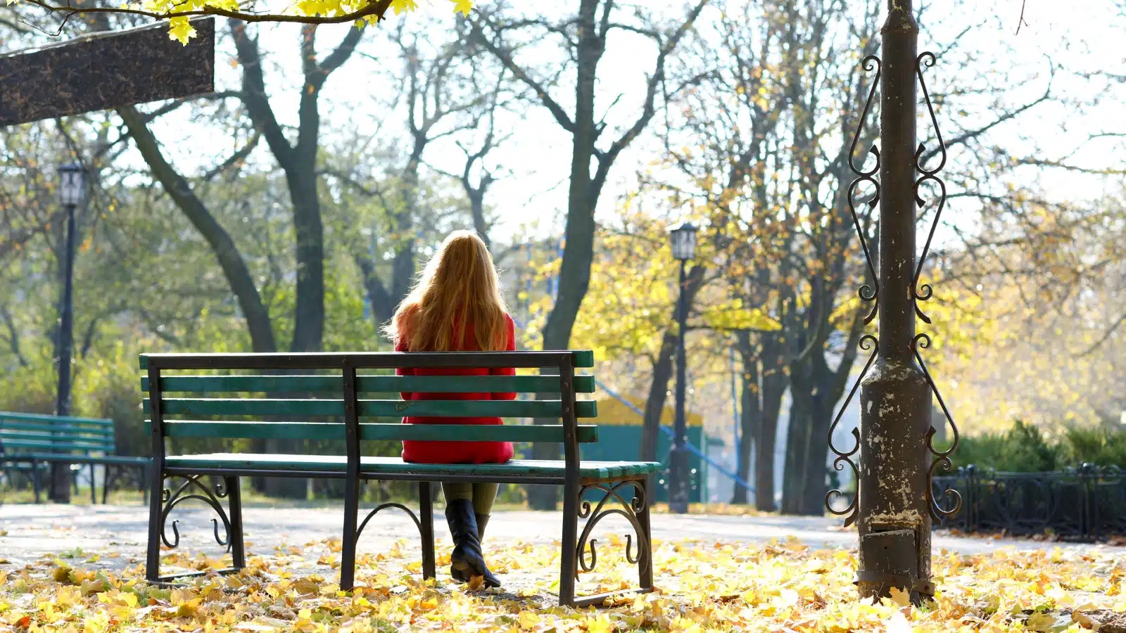 A woman sits alone on a park bench in the fall, pondering life. 