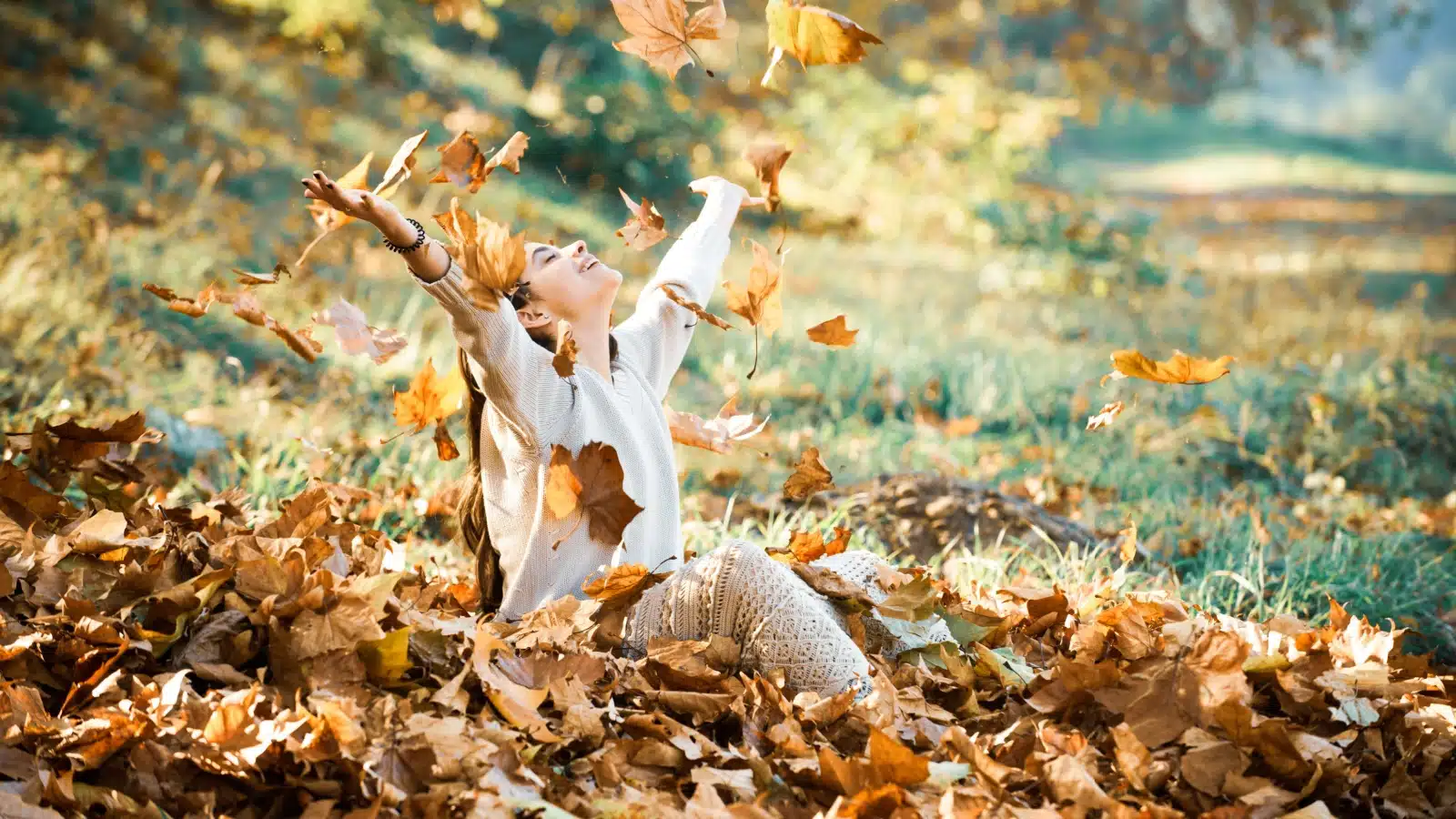 A woman throwing up fallen leaves in autumn to represent the best fall quotes.