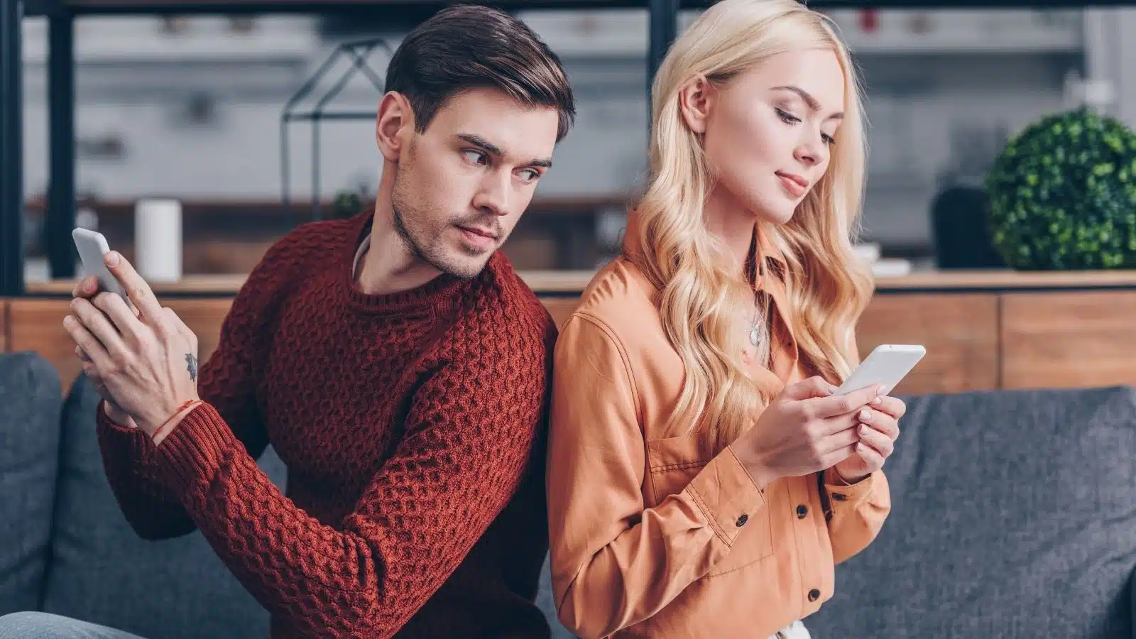 A jealous man watches his girlfriend text over her shoulder.