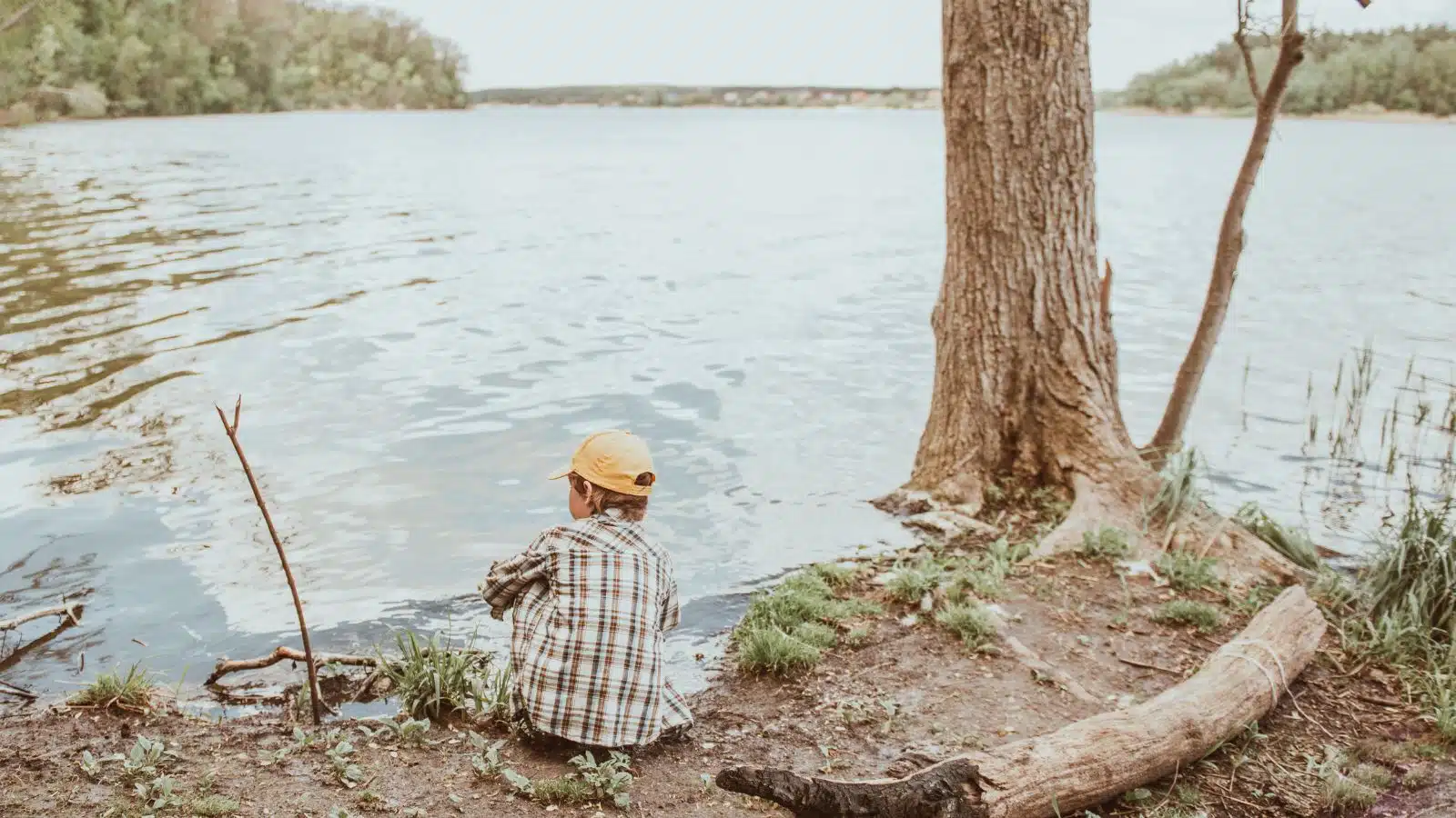 A little boy plays alone in the woods by a lake.