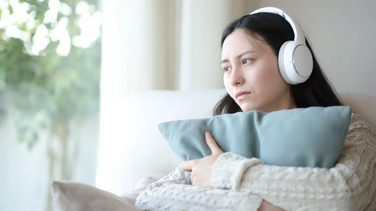 A woman hugs her pillow while listening to music to represent sad break up songs.
