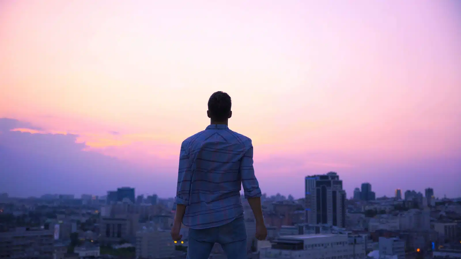 A man stands at sunrise, looking down on a city pondering his life. He's reflecting on his why, on life's meaning, and on his purpose.