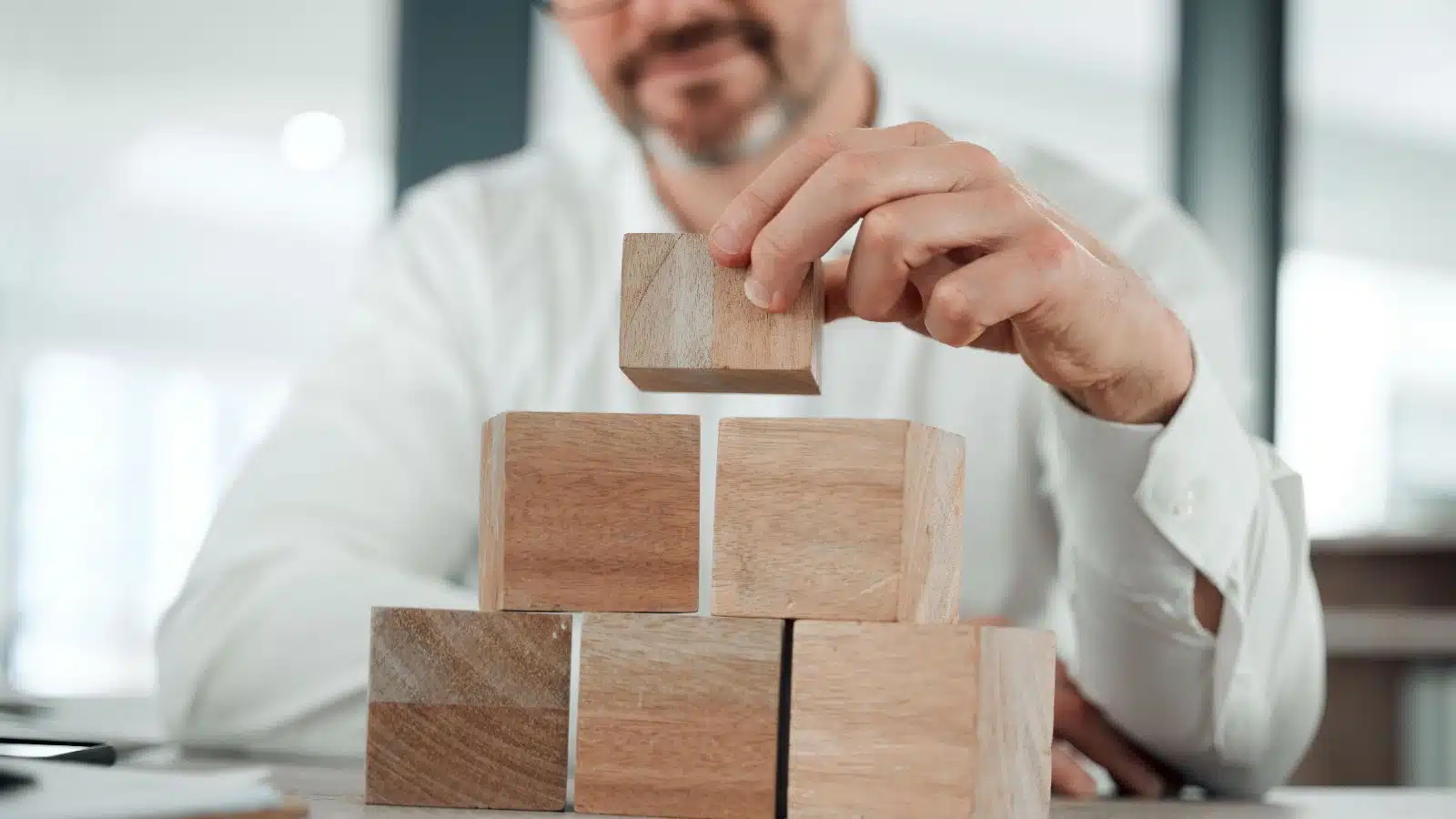 A man stacks wooden building blocks in front of himself.