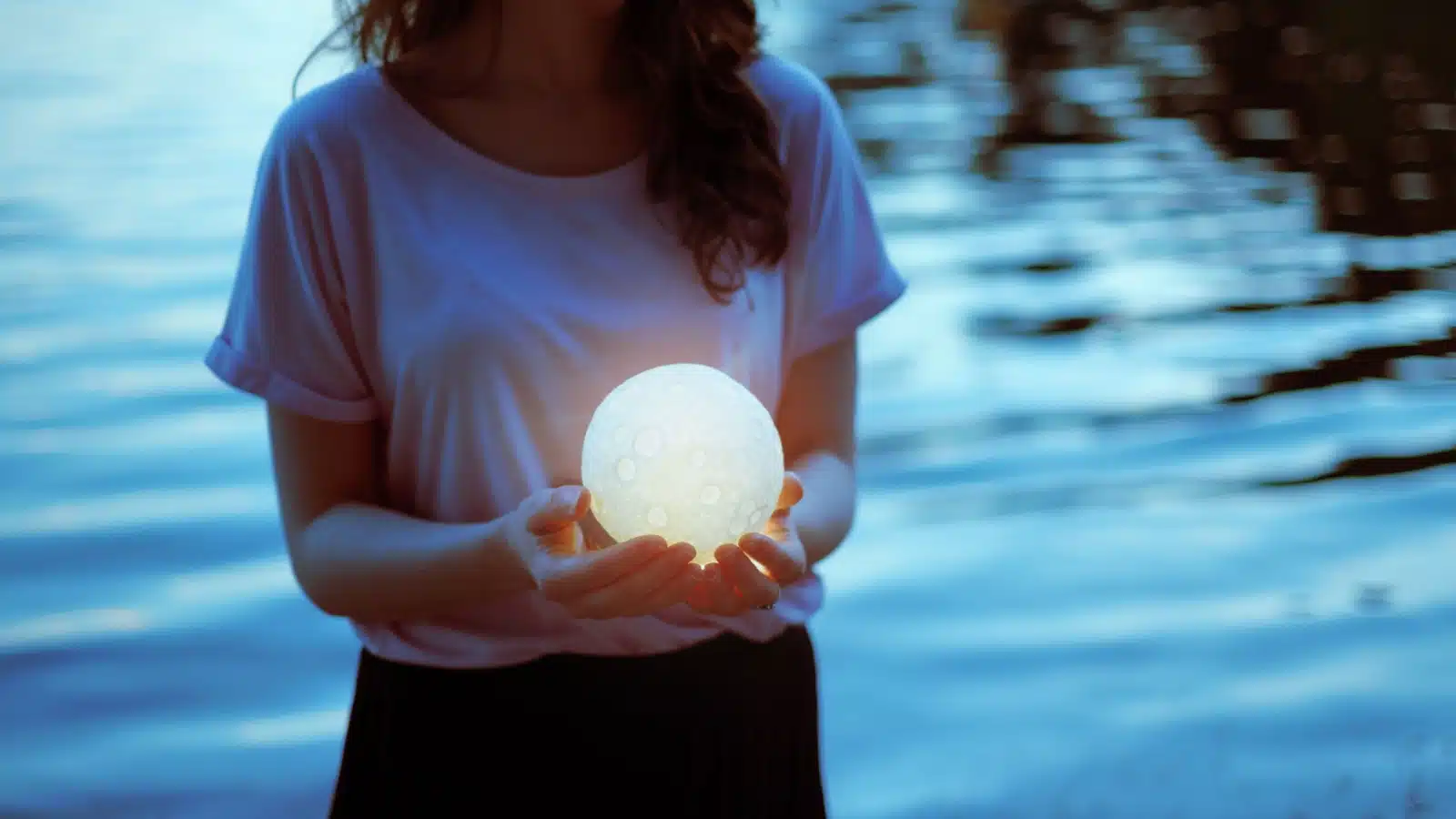 A woman holds a glowing moon in her hands to represent moon magic.