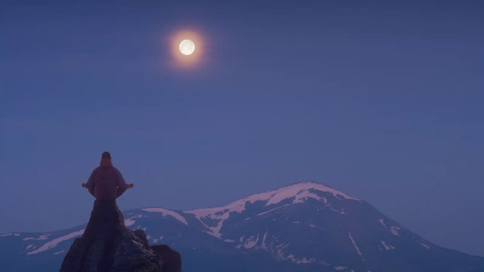 Silhouette of someone meditating on a steep cliff in the moonlight.