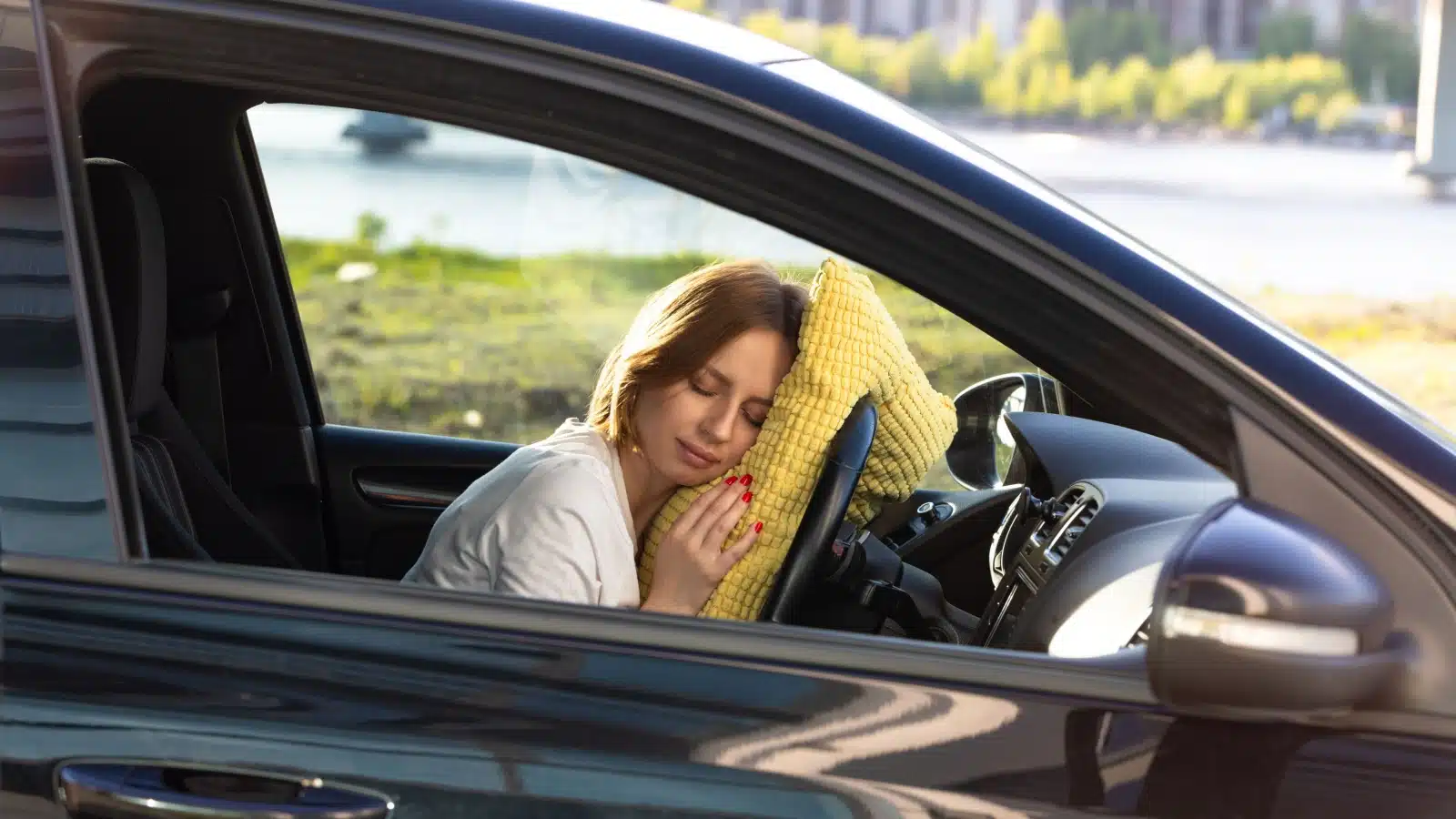 A woman sleeps in her car, resting on a pillow she placed over the steering wheel.