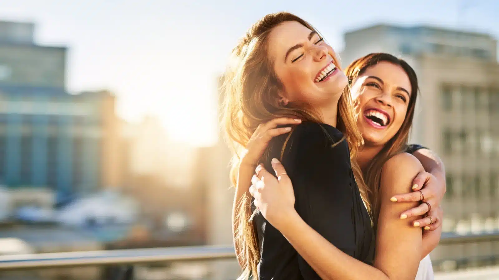 Happy friends hug with the sun shining in the background to represent how to brighten someone's day.