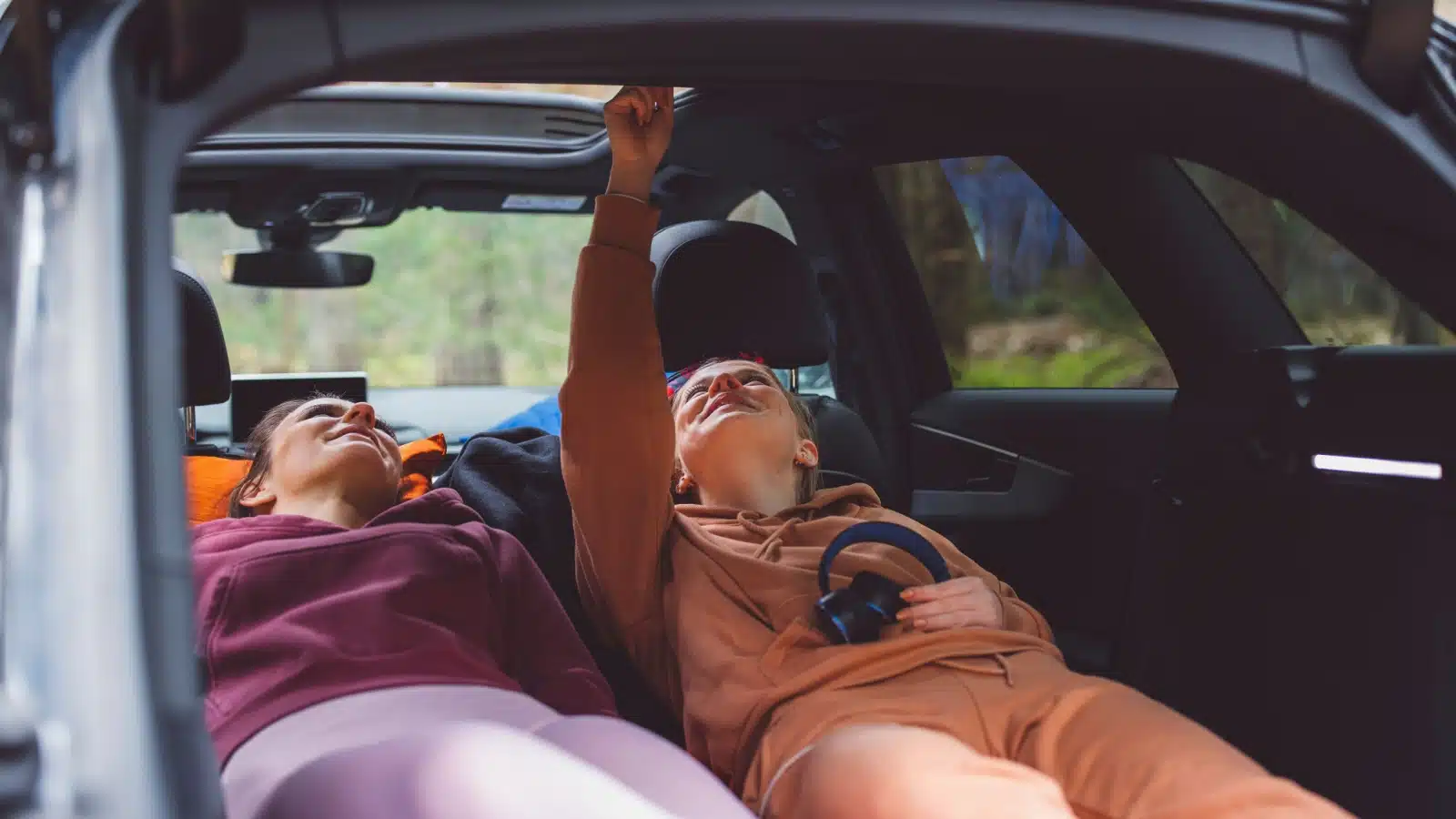 Two women car camping in the back of a roomy SUV.