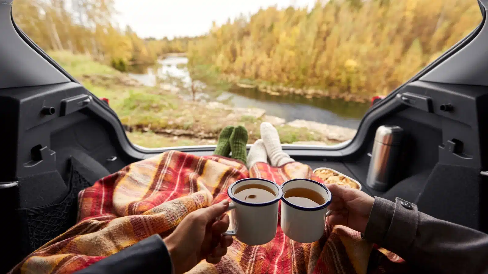 A couple enjoys a cup of coffee while snuggled up in the back of an SUV car camping.