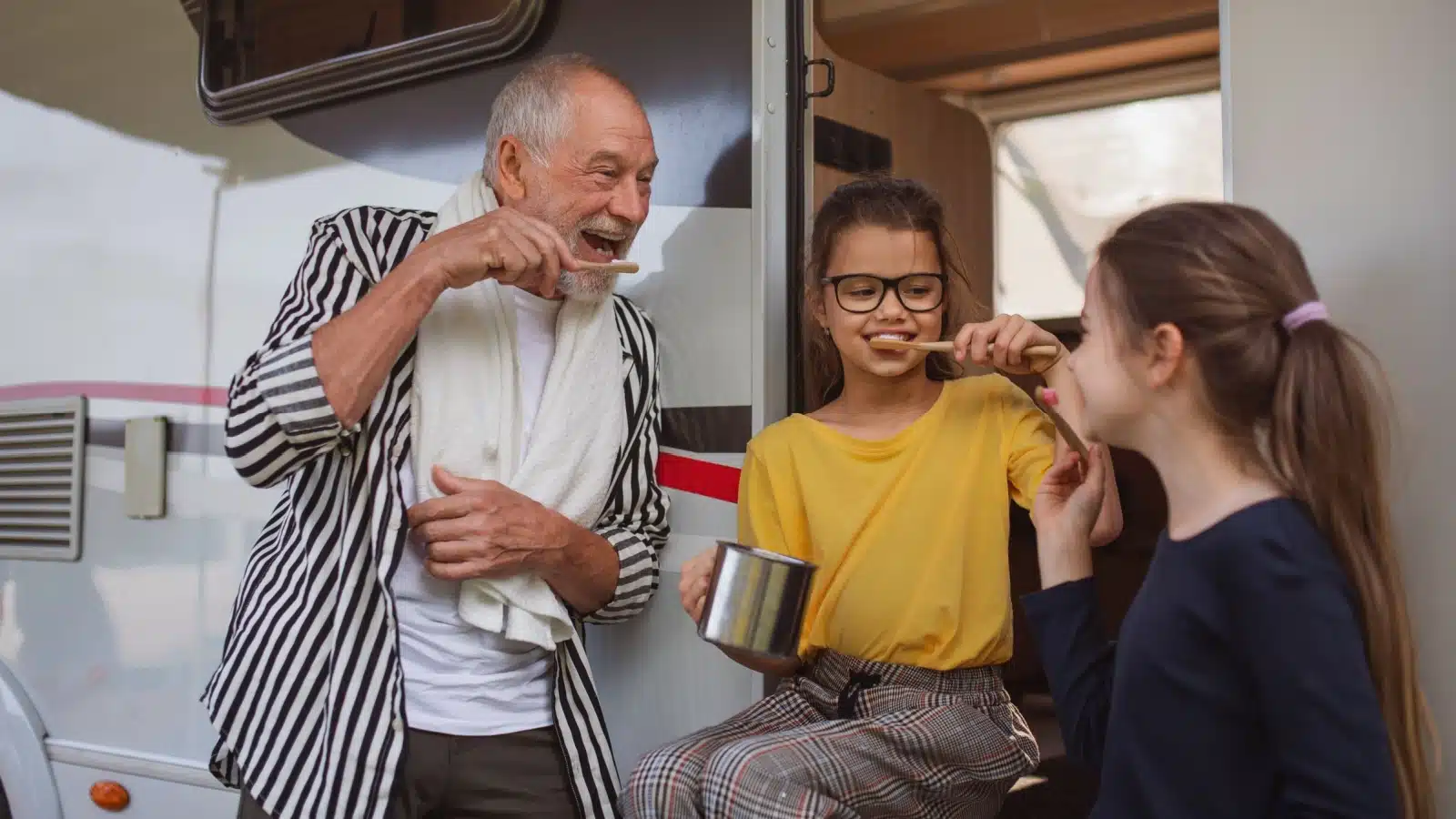 A happy family brushes their teeth together outside the RV while camping.