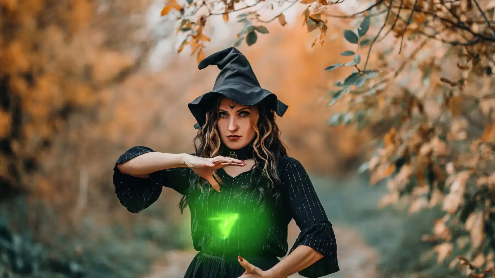 A fictional representation of spell casting. A woman dressed like a traditional witch with a pointy hat controls a green light that's hovering between her hands. 