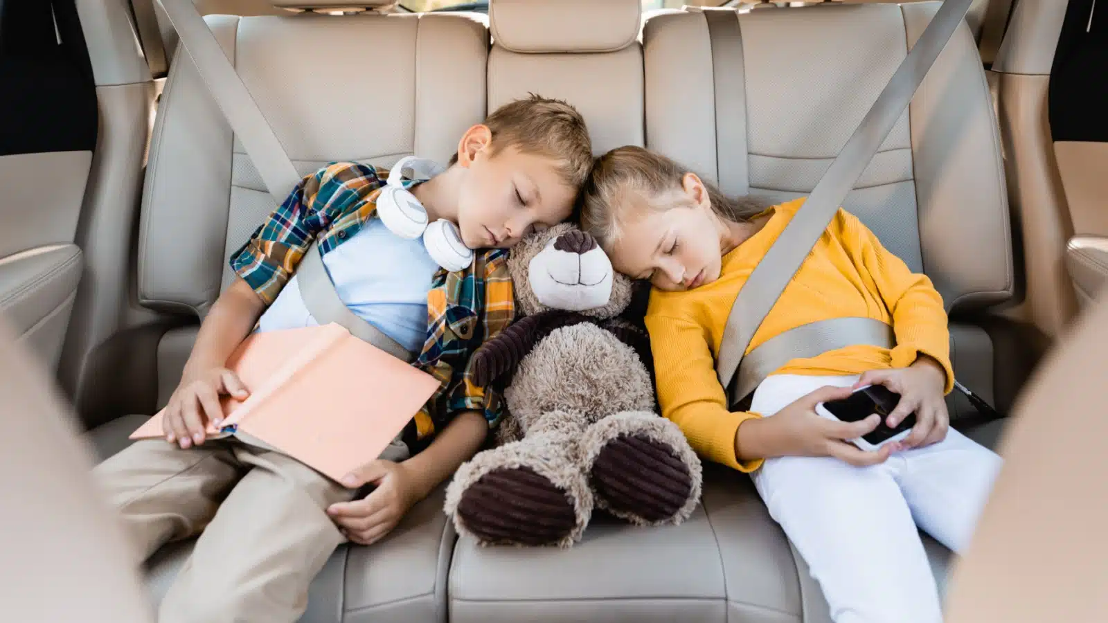Children asleep in the back seat of a car to represent how to sleep in the car on a road trip with your family.