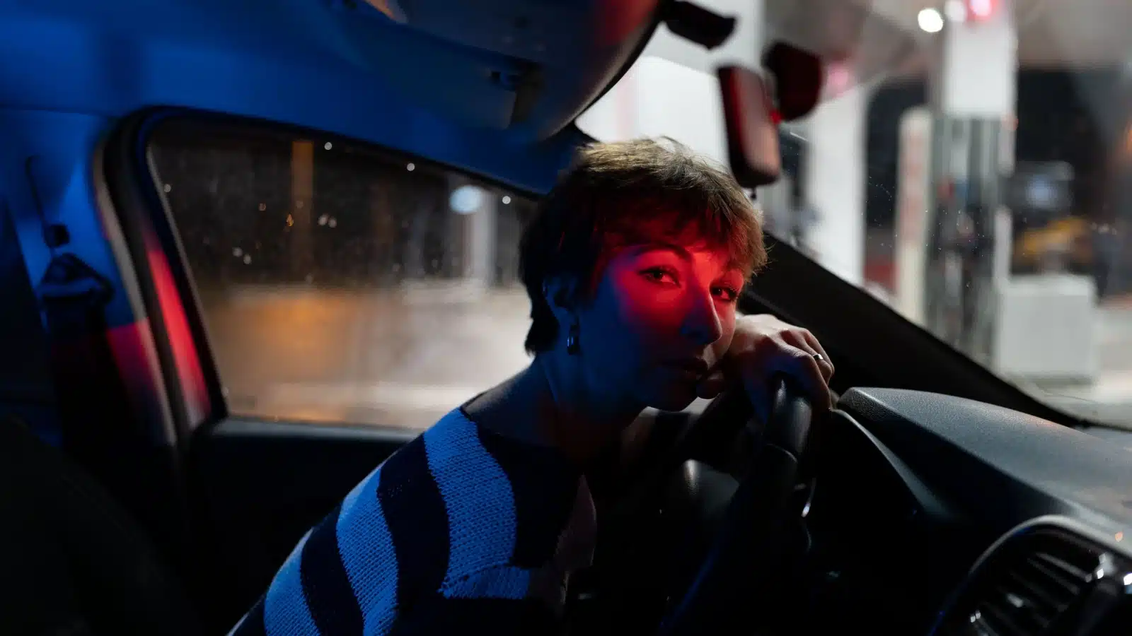 A tired woman just pulled into a gas station at night to sleep in her car safely.