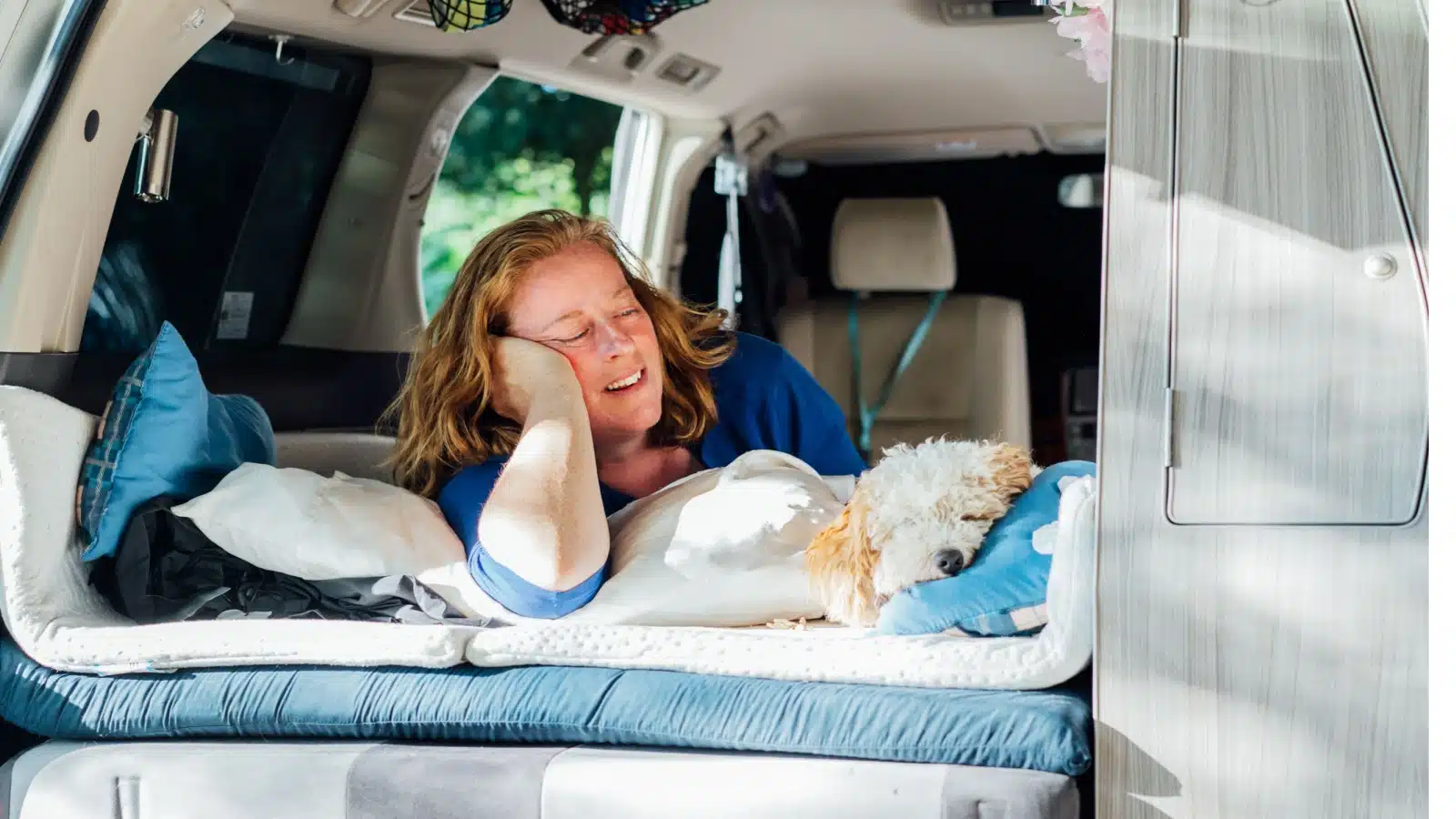 A woman sleeping in the back of a camping car with her little dog. She looks comfortable.