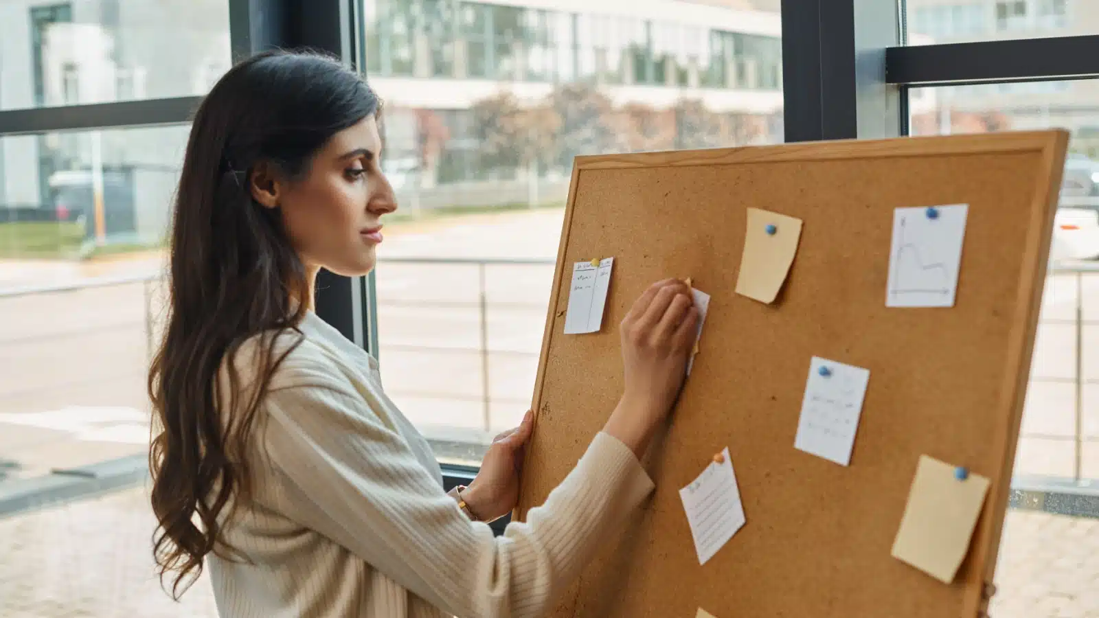 A woman uses a cork board and post it notes to set goals.