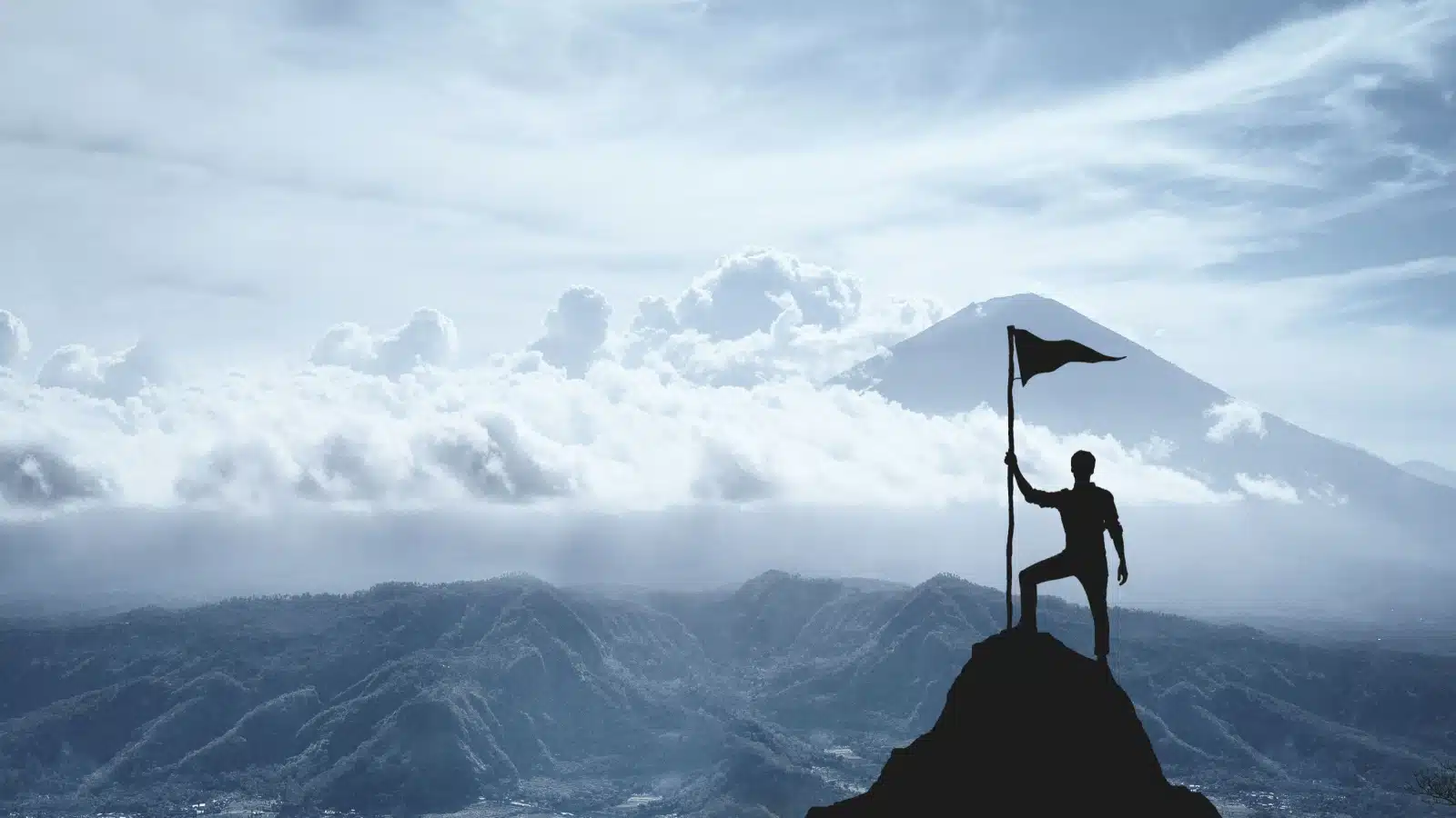 Silhouette of a man holding a flag on a mountain peak, to represent how to achieve your life goals.