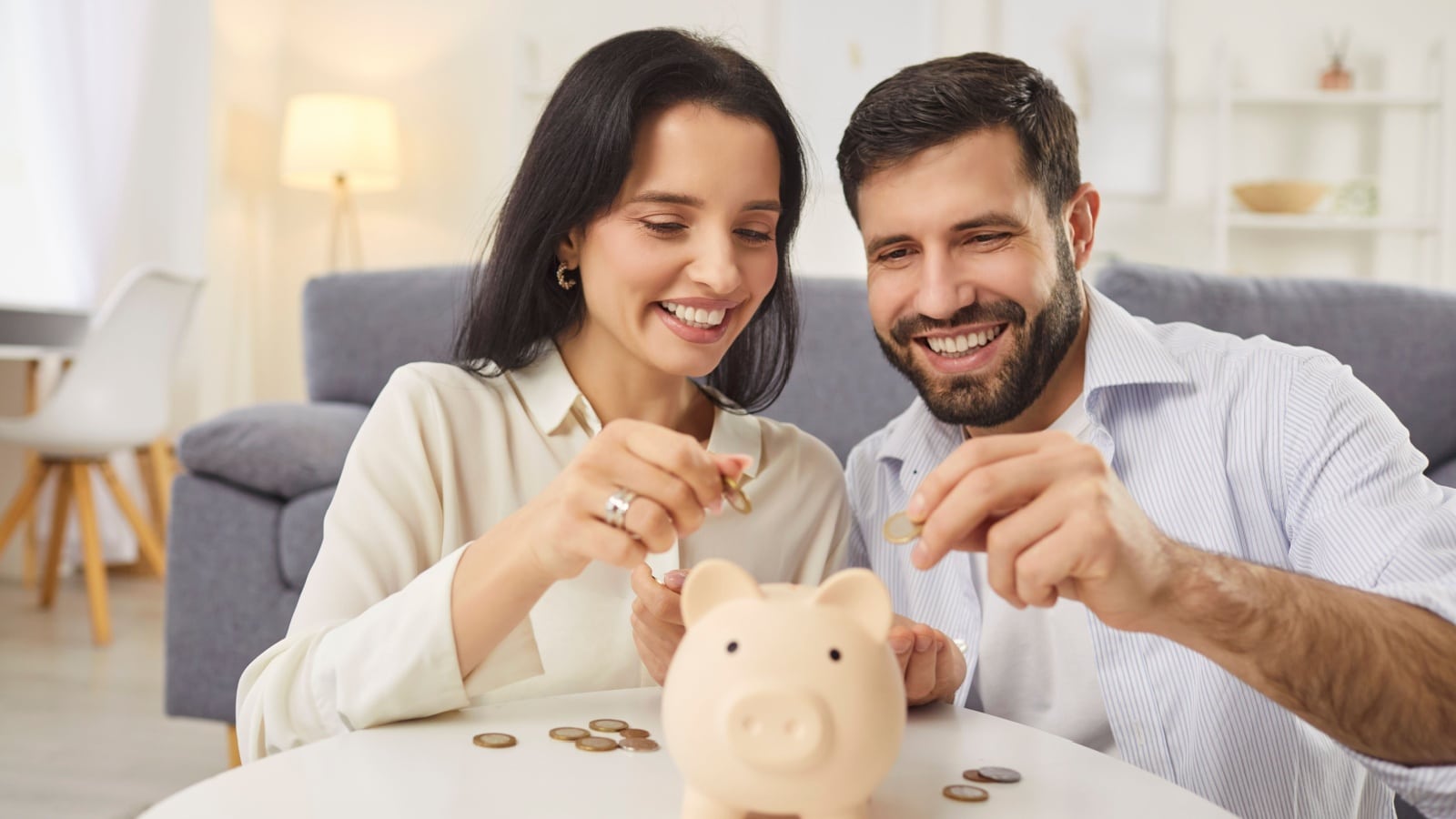 A happy couple putting money into a piggy bank together, to represent how to split costs in a relationship.