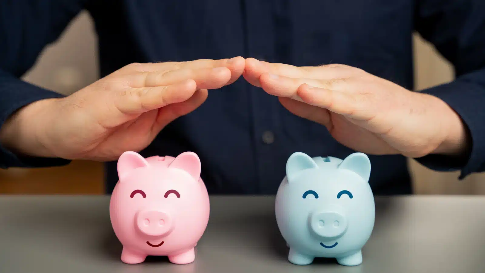 Hands over blue and pink piggy banks, to represent joining bank accounts.