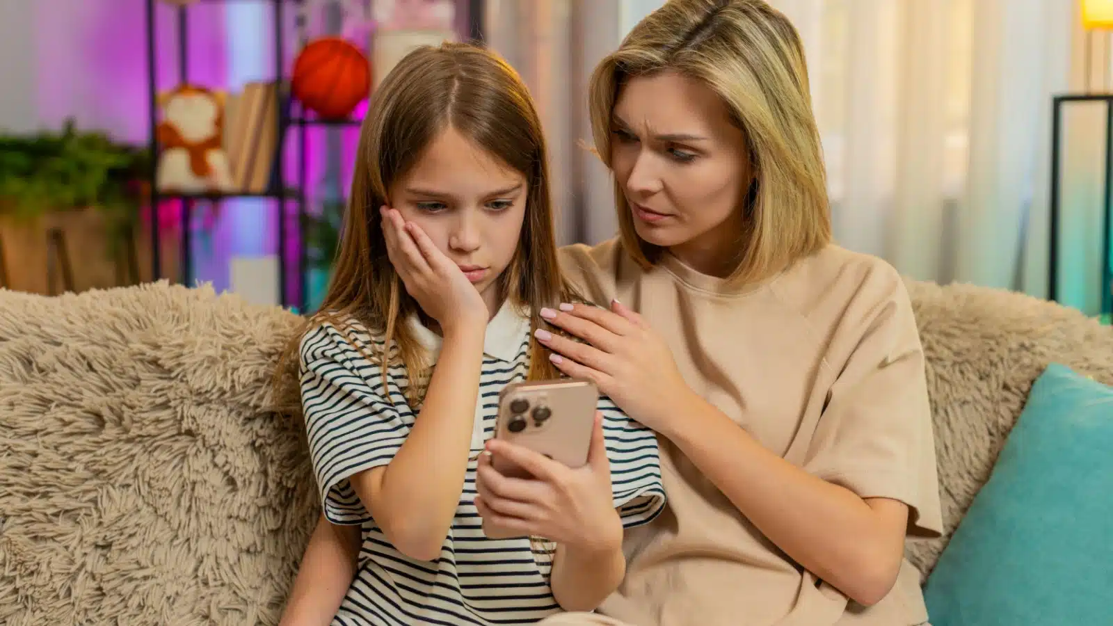 A mom comforts her daughter, who is looking sadly at her phone.