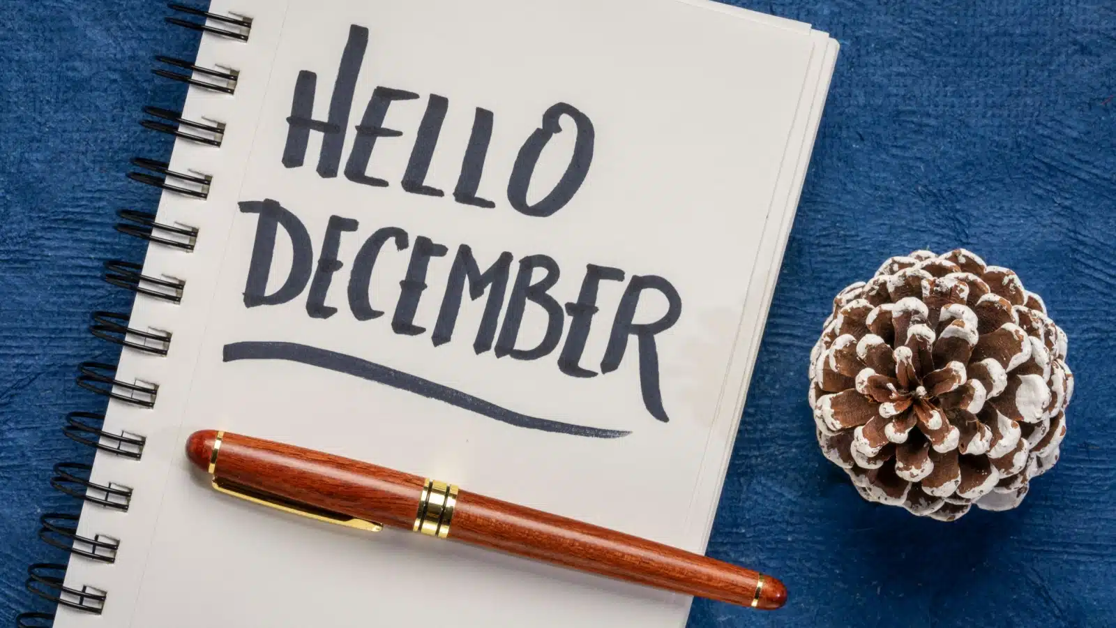 A notepad with the words "Hello December" written on it rests next to a pinecone.