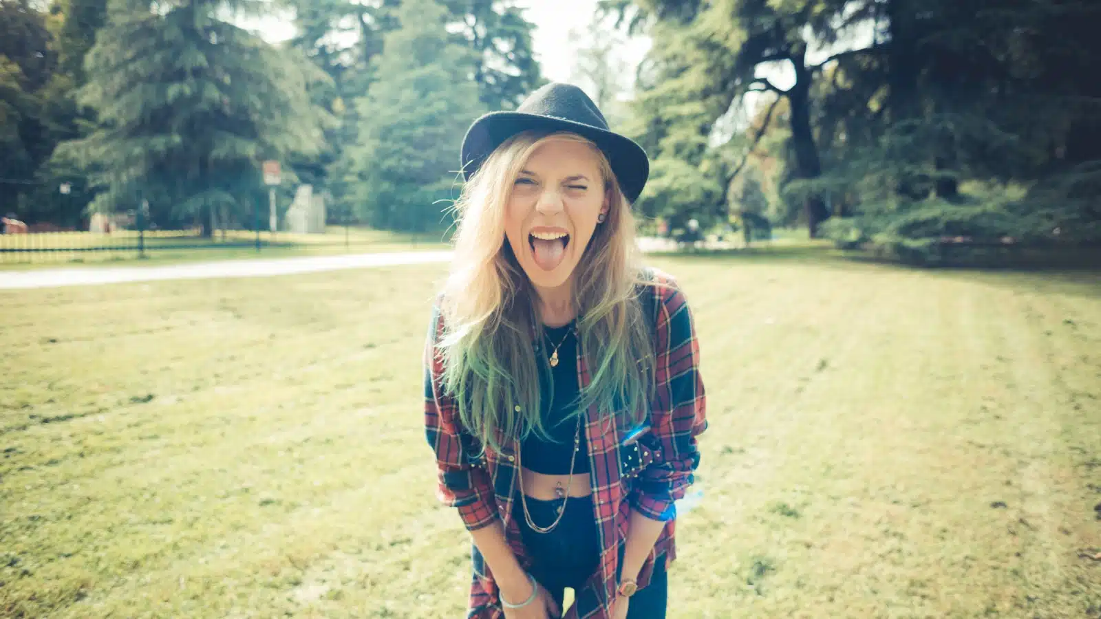 A woman dressed like a hipster is hanging out in field, making a funny face, representing how to be yourself.