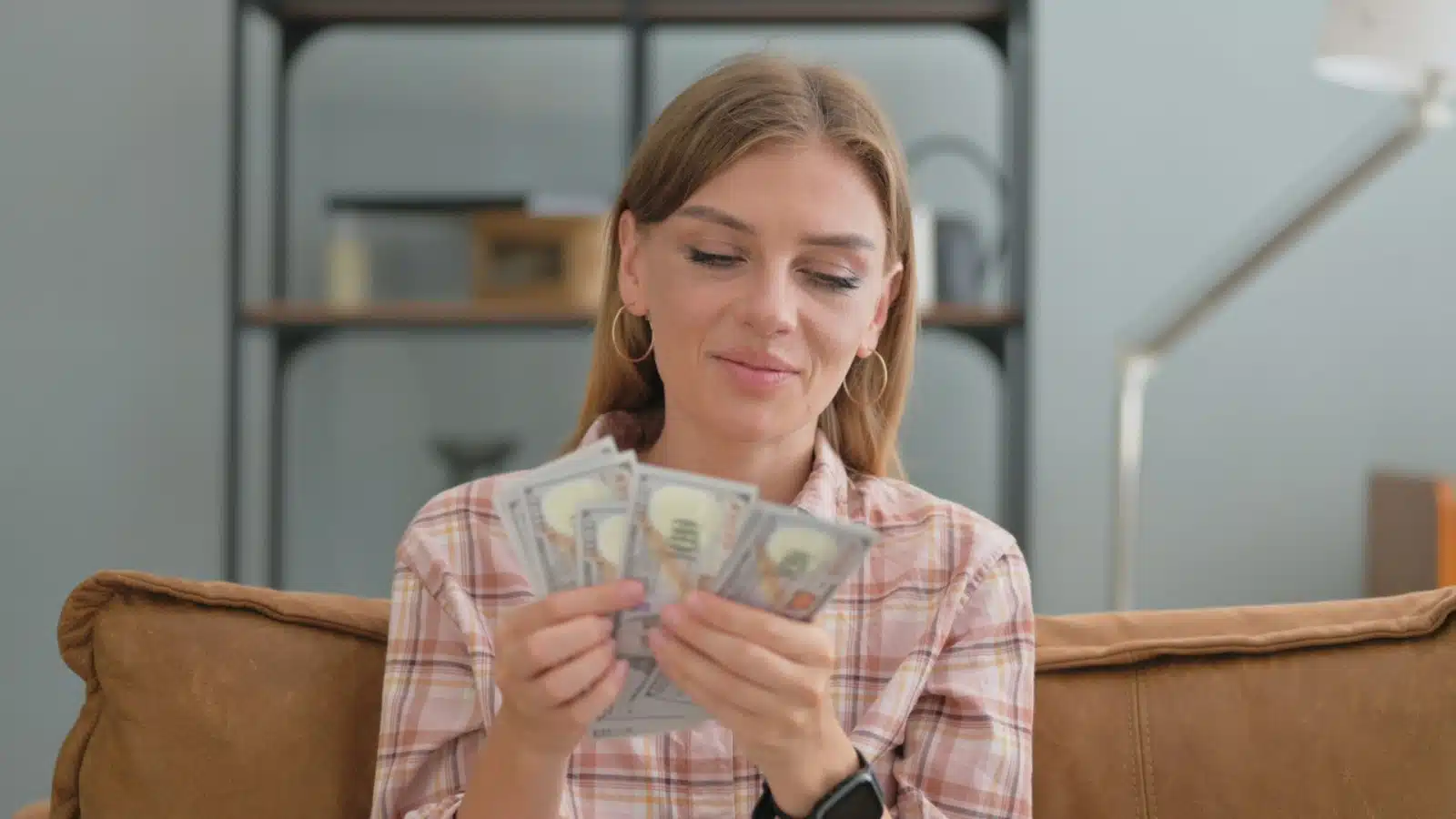 A woman counts cash on her couch, to represent how to make extra money at home.