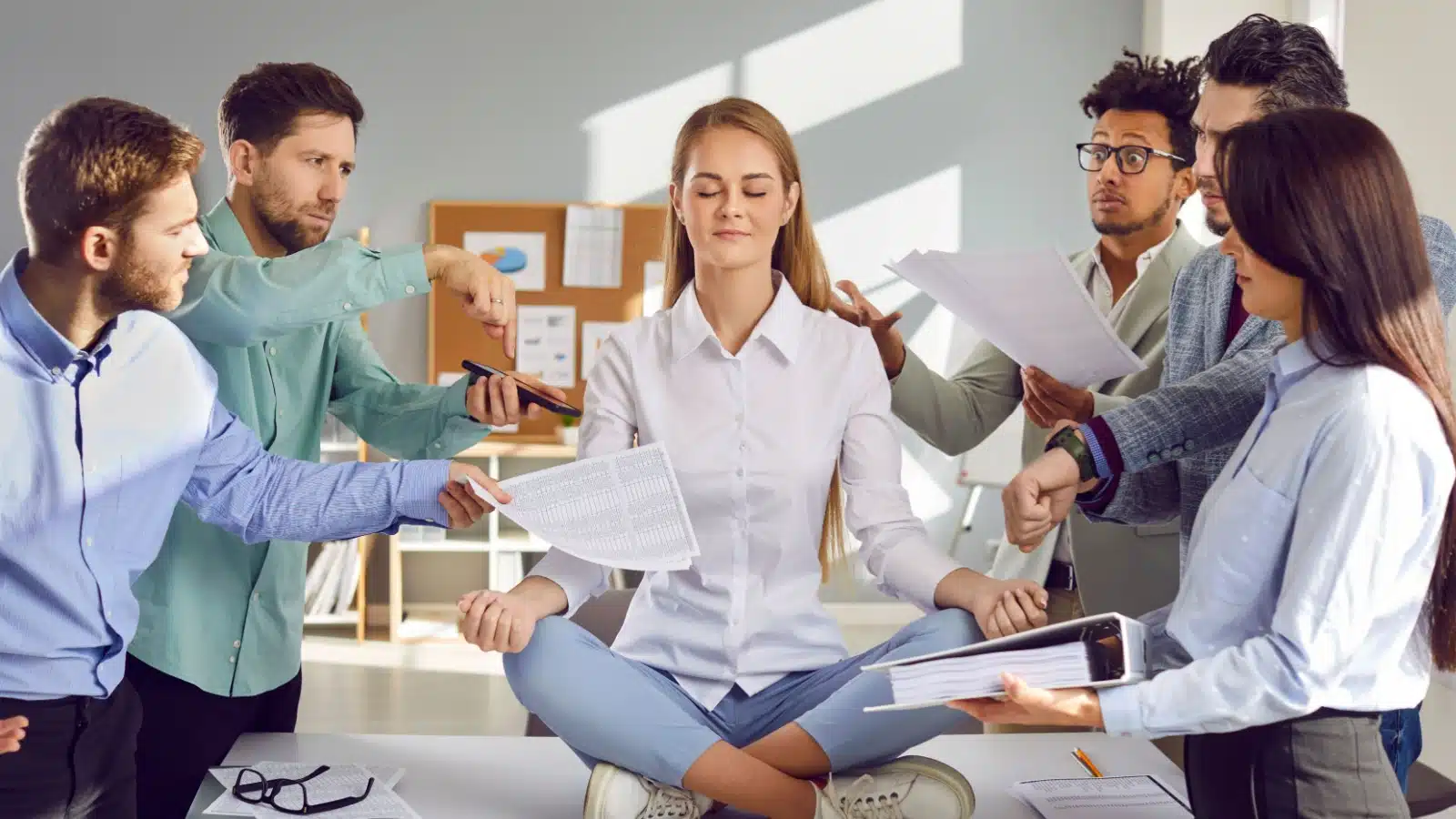 A calm woman meditating at work, ignoring all her coworkers who need something from her.