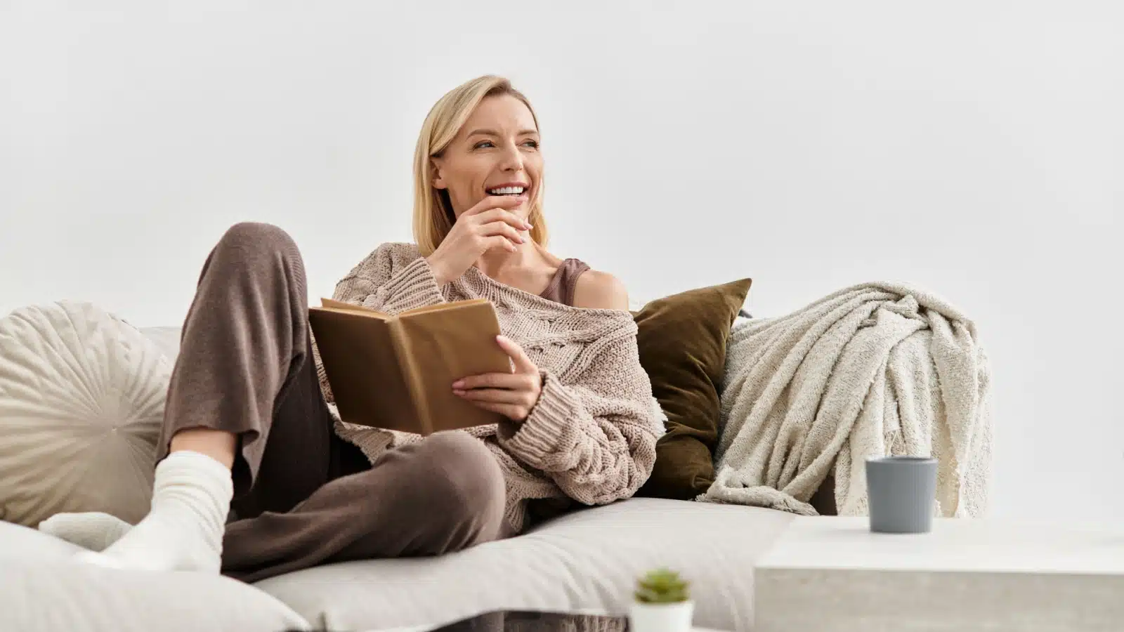 A happy woman relaxes on her sofa with a book. 