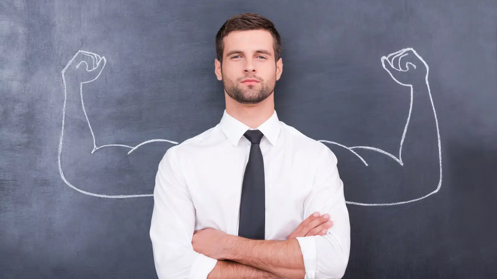 A man stands in front of a chalkboard with his arms folded, but a drawing behind him reveals hidden strengths, as it features arms flexing.