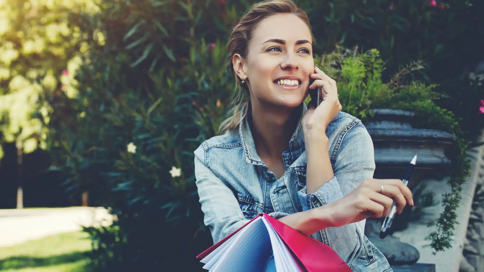 A cheerful woman talks on the phone while holding a pen and journal to represent pleasant time wasters.