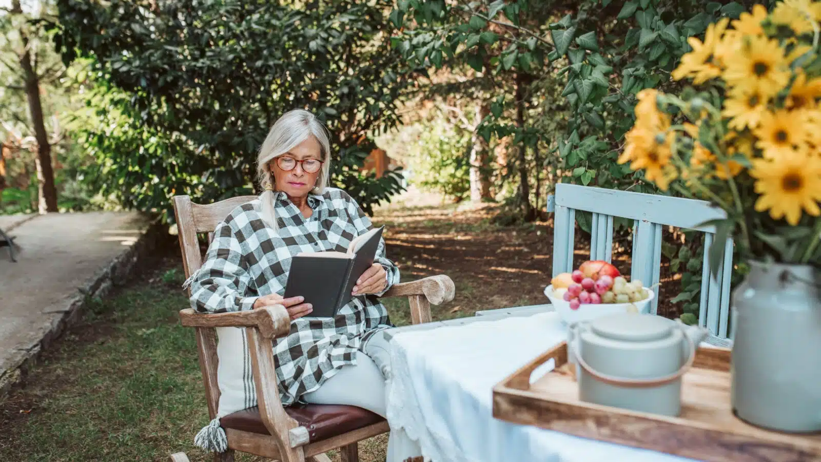 A woman enjoys a book in her rocking chair in the garden.