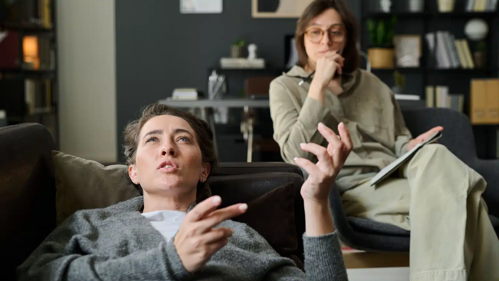 A woman talks while laying on a therapist couch while the counselor sits in the background.