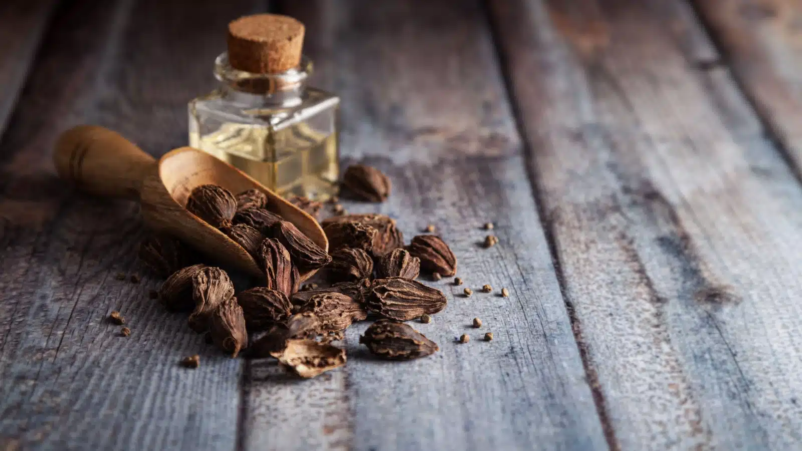 A scoop of cardamom seeds on a wooden table.
