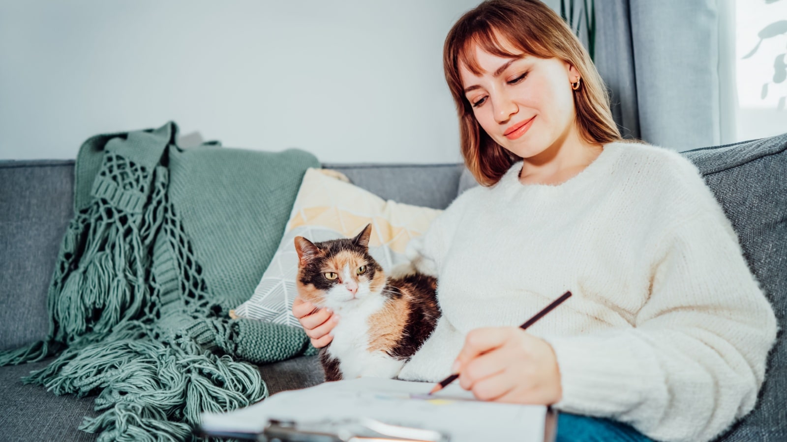 A woman sits on the couch with her cat, creating an action plan for her life.