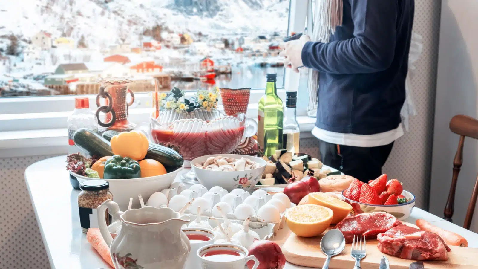 A table filled with food is in front of a window which shows a wintery landscape outside to represent winter flavors.