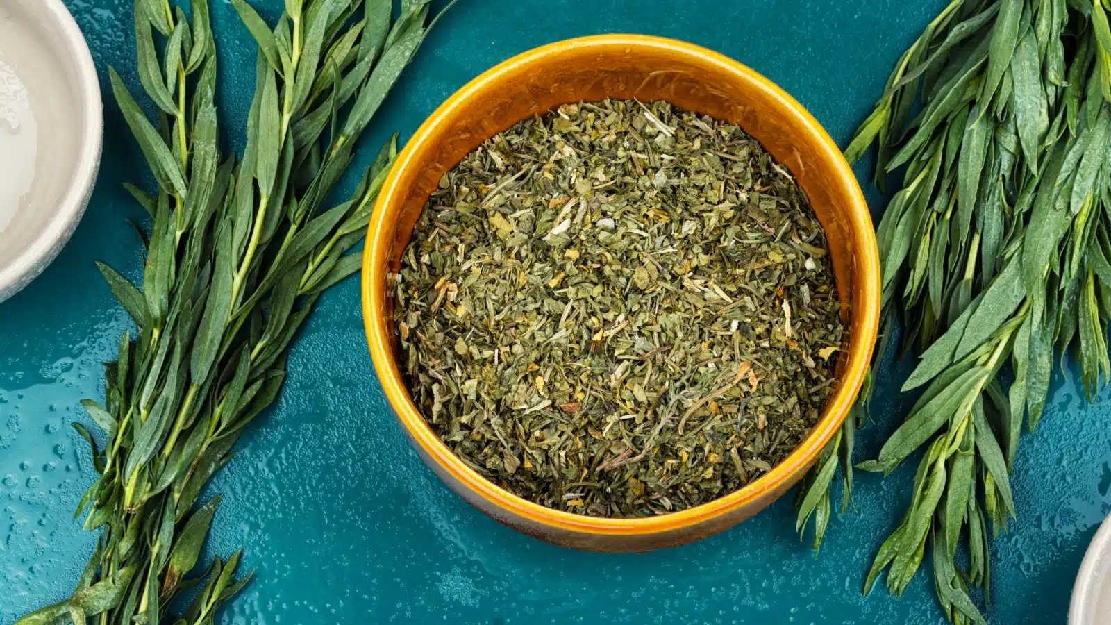 Dried tarragon in a bowl next to fresh tarragon.