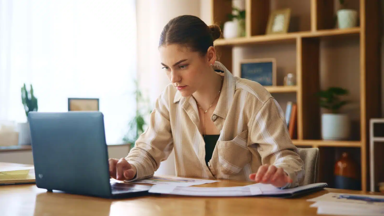 A woman reviews her finances with paperwork and her laptop to represent budgeting methods.