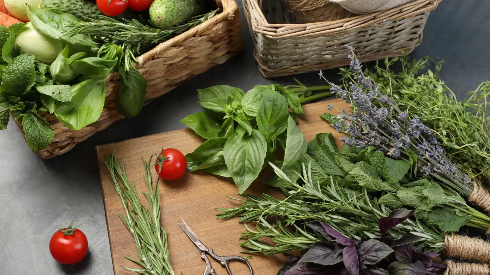 A cutting board and basket filled with fresh spring bounty with includes herbs and vegetables. 
