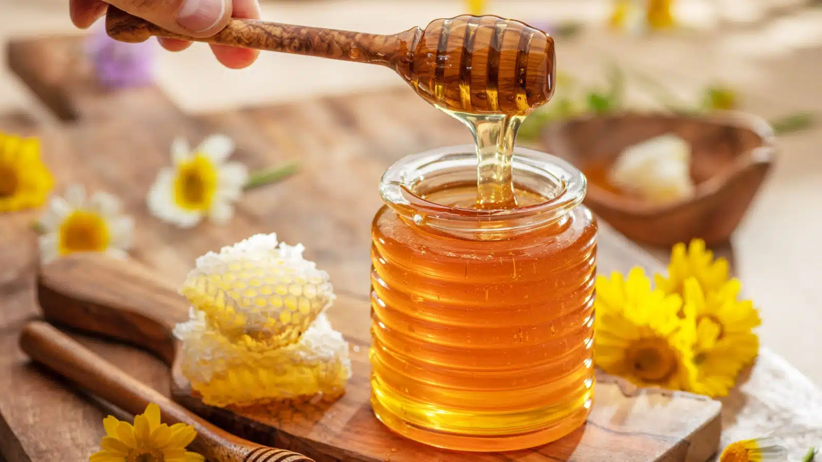 Fresh honey being lifted from a jar with a honey spoon.
