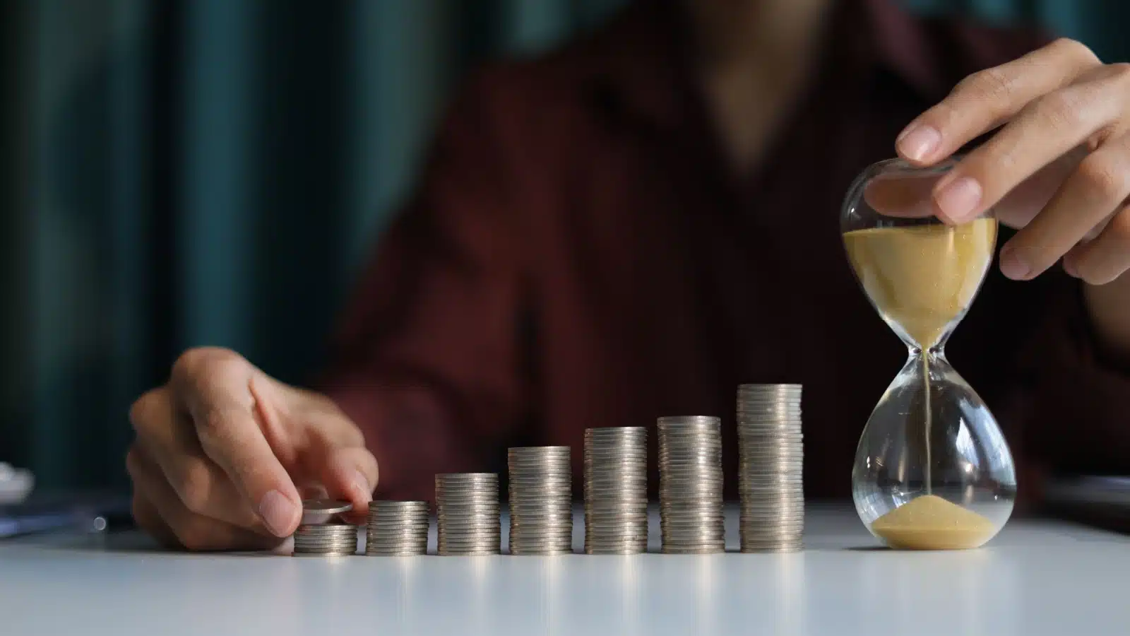 A rising stack of coins next to an hour glass highlight the power of compound interest.