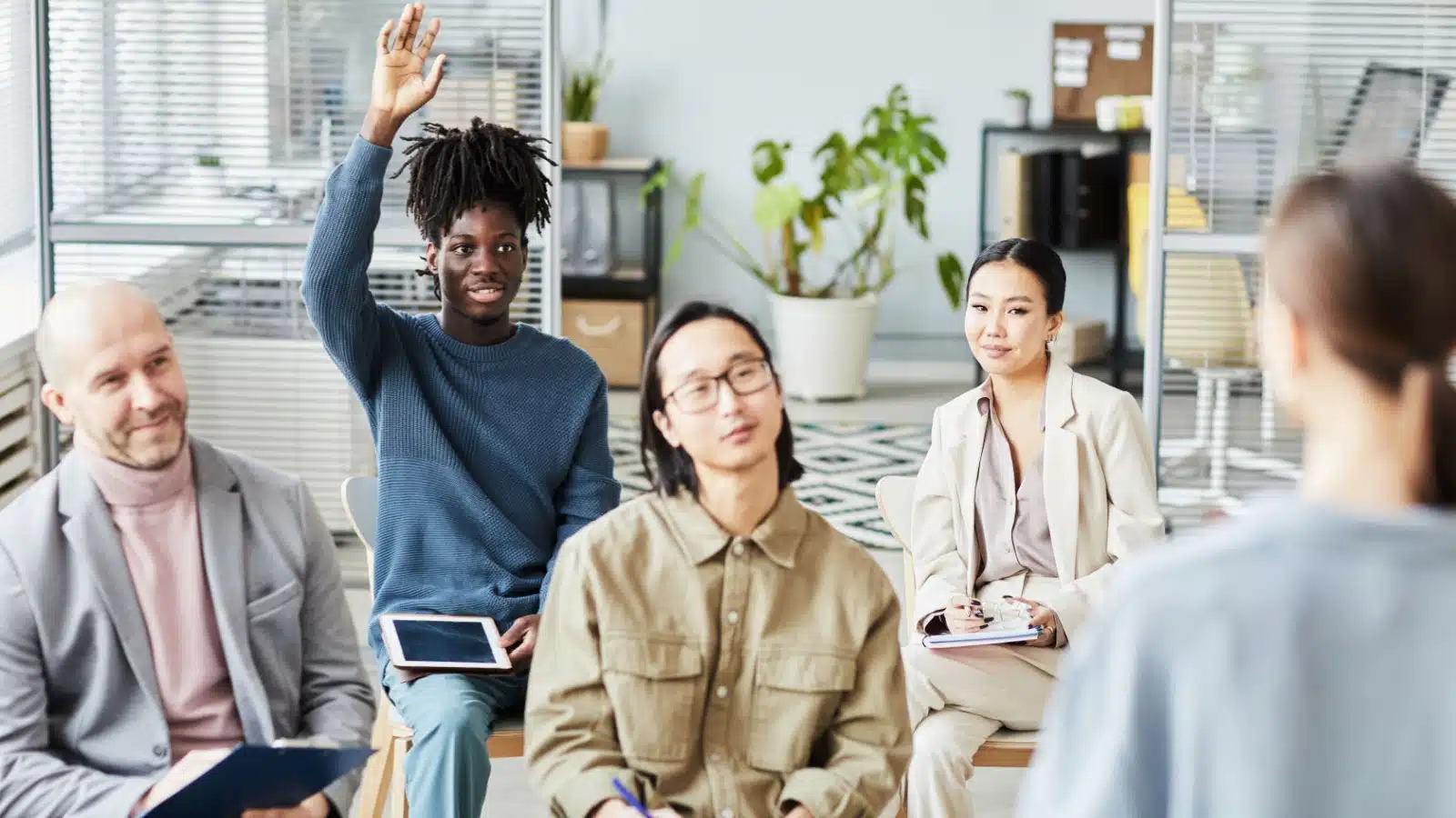 A young employee raises his hand to ask a question in a group mentorship session.