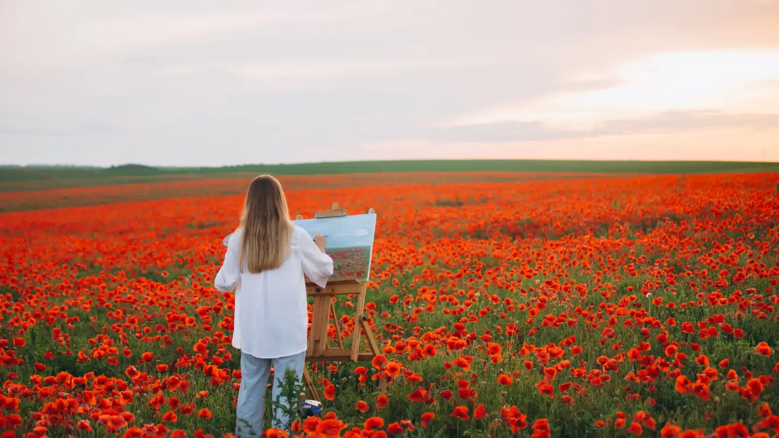 A woman plein air painting in a poppy field.