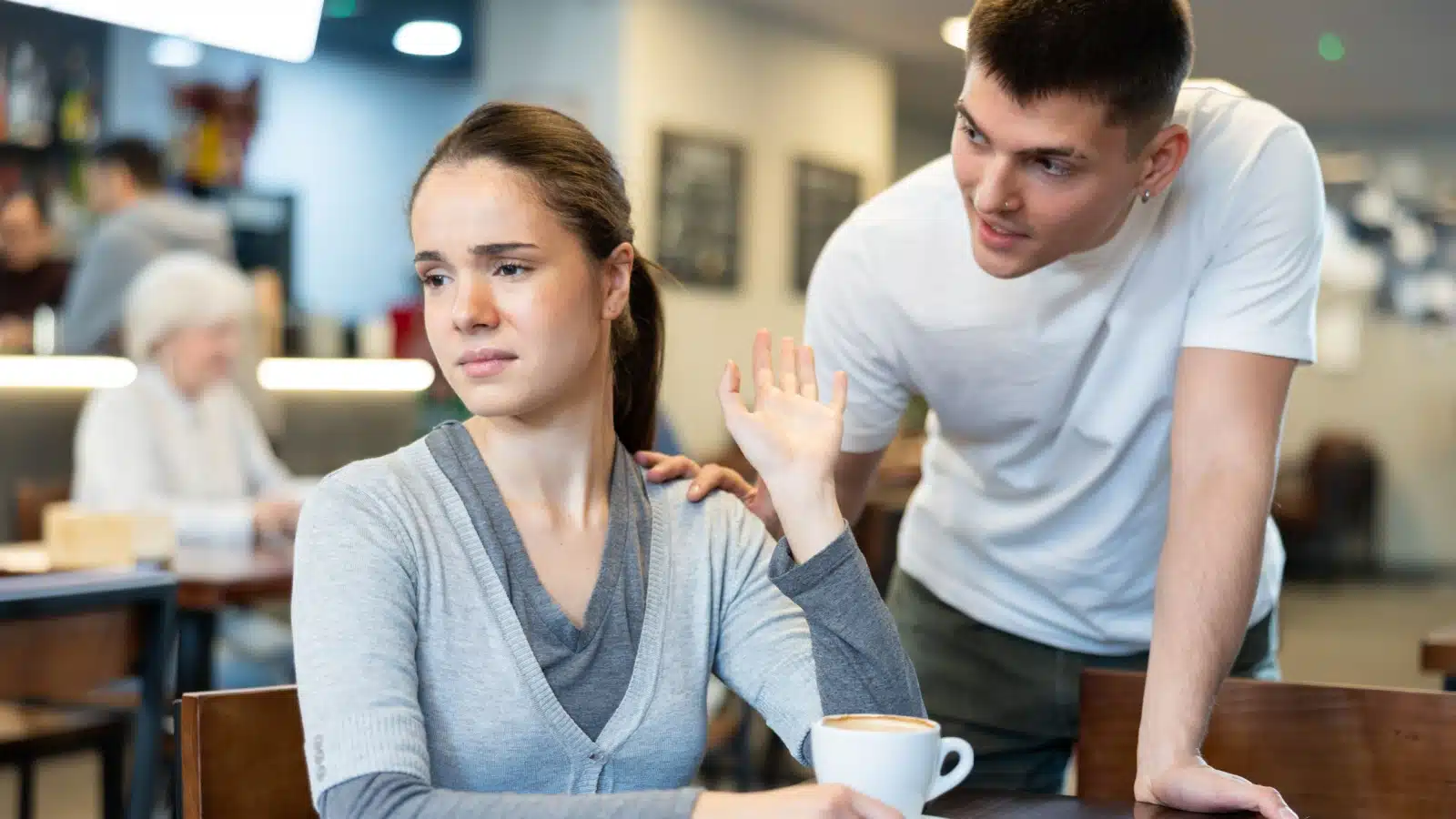 A man touches a women's shoulder uncomfortably while trying to get her attention to highlight women's struggles with dating.