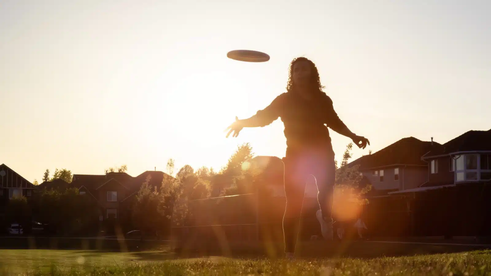 A woman plays frisbee at sunset.